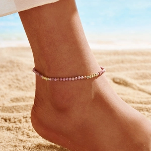 Detailed view of silver anklet with purple natural stones and engraved gold beads on beach