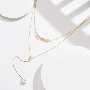 Detail of gold layered necklace with pearls and a pear-cut zircon pendant on white tray