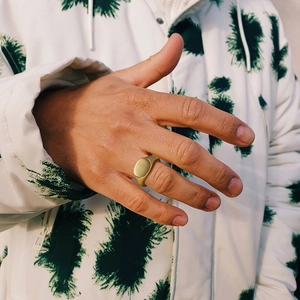Macro shot of minimalist gold signet ring on finger with street style background