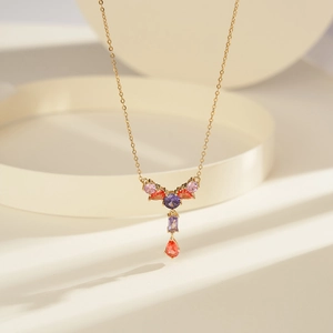 Elegant gold pendant necklace with purple and orange gemstones on beige circular display