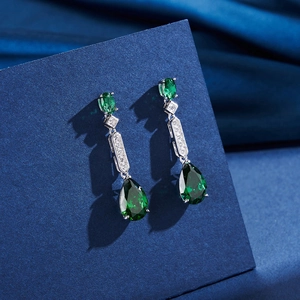 Detailansicht von Smaragd-Ohrhängern mit Zirkon auf blauem Seidenhintergrund