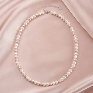 Macro shot of colorful pearl necklace with silver lobster clasp on pink satin fabric