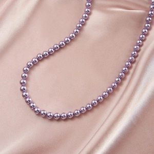 Macro shot of lavender pearl necklace on pink silk fabric showing lustrous round beads