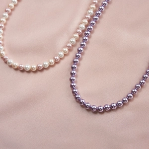 Elegant purple and pink pearl necklace set displayed on smooth pink silk fabric