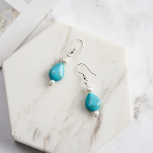 Detailed view of turquoise teardrop earrings with white pearls on marble surface