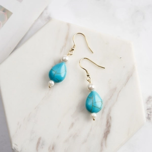 Detail of teardrop turquoise earrings with white pearls and gold hooks on marble