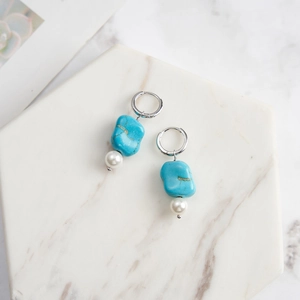Détail de boucles d'oreilles turquoise et perles sur support en marbre blanc élégant