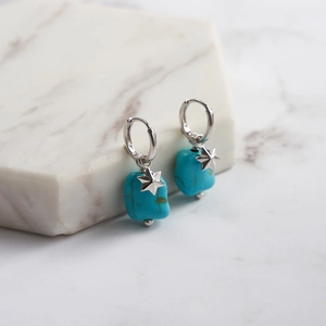 Detailed close-up of S925 silver turquoise star earrings on a white marble surface