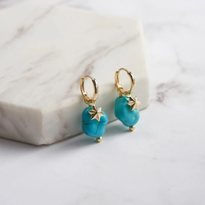 Detail of star-studded turquoise stone charms on gold hoops over marble background