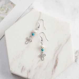 Detail of silver drop earring with pearl, turquoise bead and infinity knot on marble tray
