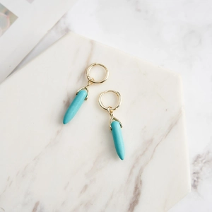Bullet-shaped turquoise drop earrings with gold hoops on a marble surface