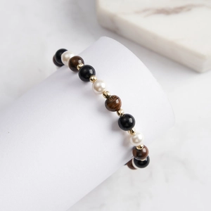 Detail of beaded bracelet with tiger eye stones, black obsidian, and white pearls on a white stand