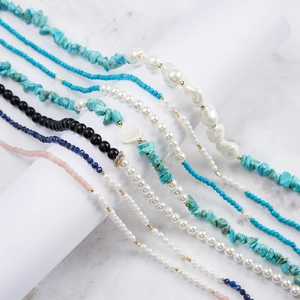 Detail of layered jewelry with turquoise stones, baroque pearls, and shell heart charms