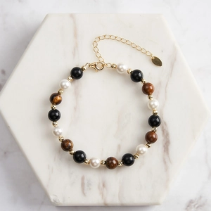 Detail of beaded bracelet with tiger eye stones and gold lobster clasp on marble