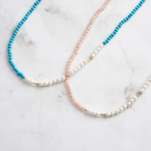 Close-up of pink and blue faceted bead necklaces with white pearls on marble