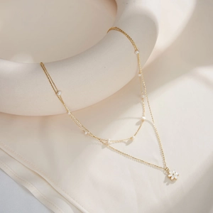 Close-up of double-layer gold chain necklace featuring small pearls and a white flower pendant