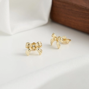 Macro detail of 3D gold ribbon bow earrings with realistic texture and metallic shine