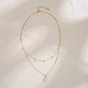 Detail of gold double-layer necklace featuring small pearls and a floral petal pendant