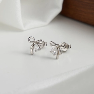 Macro shot of silver bow stud earring featuring a drop-cut zircon on white stone