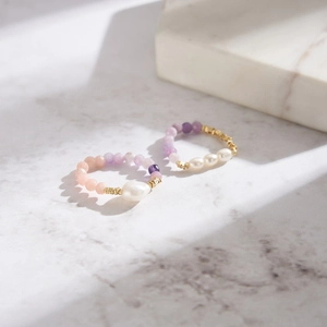 Detail of beaded rings with freshwater pearls and pink opal on marble surface