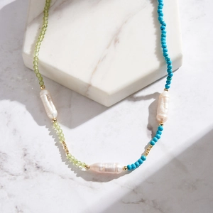 Macro shot of baroque pearls and green turquoise beads on a white marble display