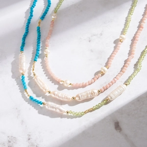 Détail de colliers en perles naturelles et pierres pastel sur fond de marbre