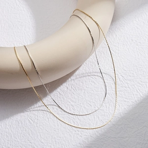 Minimalist sterling silver and gold snake chain necklaces displayed on elegant stands