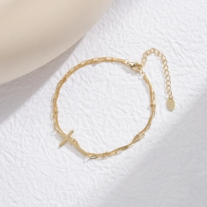 Macro detail of gold S925 sterling silver layered chain bracelet with a cross charm