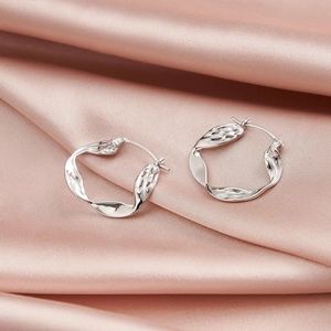 Detail of silver twisted hoop earrings with wavy texture on pink silk fabric