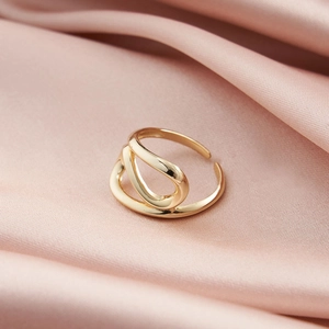 Detailansicht des verschlungenen goldfarbenen Rings auf rosa Seidenhintergrund