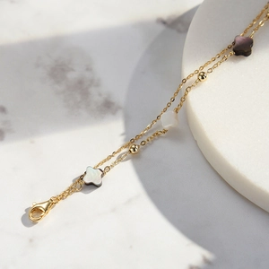 Elegant gold double-chain bracelet with black and white clover shell charms on marble