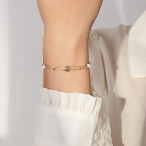 Close-up of double-layered gold bracelet with clover pendant and white pearls on wrist