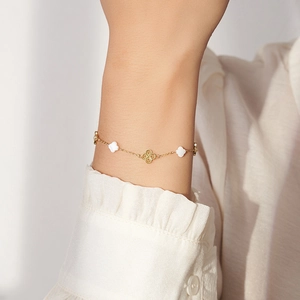 Detailansicht eines goldenen Kleeblatt-Armbands mit weißem Perlmutt am Handgelenk