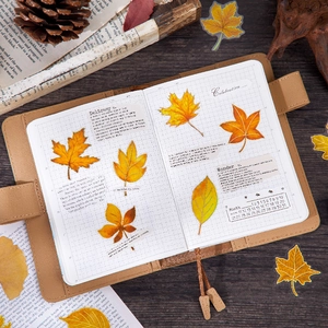 Brown leather notebook with autumn maple leaf stickers on a vintage wooden background
