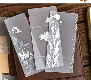Close-up of translucent botanical scrapbooking paper with white floral prints on leather journal