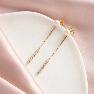 Macro detail of S925 silver pearl drop earrings with long gold chain and pave zircons