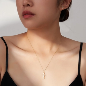 Detail of a woman wearing a gold S925 silver cross necklace and pearl earrings set
