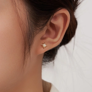 Elegant gold starburst stud earrings with natural white pearl on female model ear