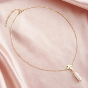 Detailed view of golden cross necklace with baroque pearl on pink silk fabric
