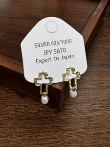 Détail de boucles d'oreilles croix en argent S925 avec perles sur présentoir en bois