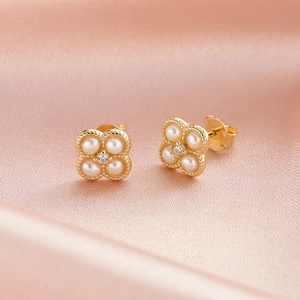 Détail macro de boucles d'oreilles trèfle avec perles blanches et bords perlés dorés