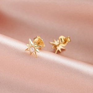 Elegant gold octagram star earrings with white natural pearls on pink satin background