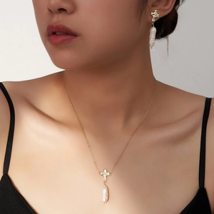 Detailed view of model wearing gold cross necklace with baroque pearl and matching earrings