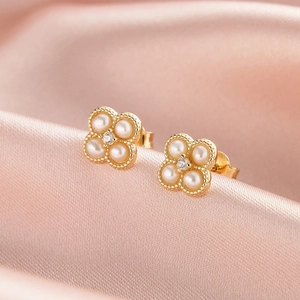 Gros plan de boucles d'oreilles trèfle en perles et zircon sur satin rose