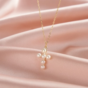Elegant gold cross necklace with six small white pearls on pink satin background