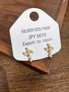 Detail of cross-shaped pearl earrings on a Silver 925 card inside a dark wooden tray