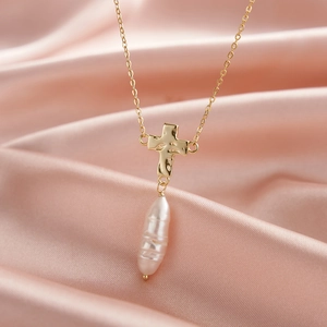Golden cross necklace with baroque pearl pendant on pink silk background