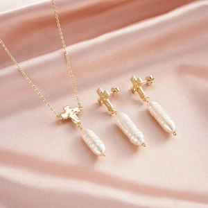 Detailed view of baroque pearl cross necklace and earrings set on pink silk fabric