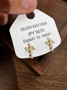 Detail of S925 silver cross pearl stud earrings on a display card with natural lighting