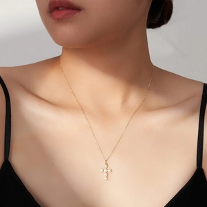 Elegant gold cross necklace with white pearls worn by a model to show refined collarbone fit